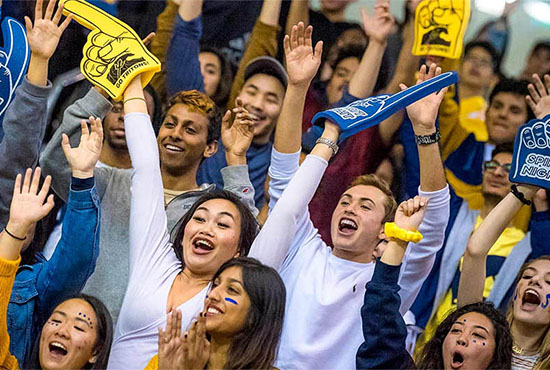 UC San Diego students dressed in blue and gold stand and cheer in the RIMAC stands during Spirit Night