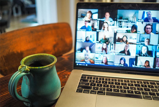 Laptop next to coffee mug; computer screen displays several people in separate online chat windows. Photo by Chris Montgomery on Unsplash.com.